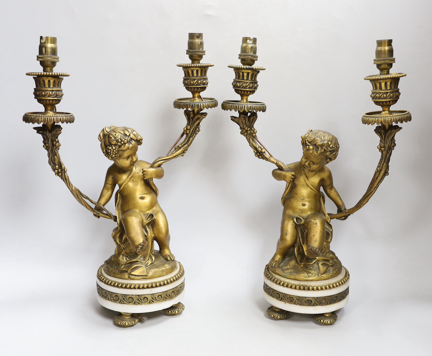 After Clodion (1738 –1814) Pair of two branch gilt bronze candlesticks in the form of Putti, each raised on circular bases, 34cm high